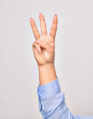 Beyaz arka planda uzanmış parmaklarıyla üç numarayı gösteren beyaz bir kadının eli.