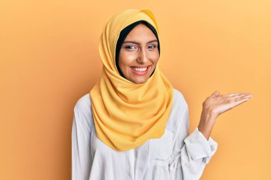 Genç esmer Arap kadın geleneksel başörtüsü takıyor neşeli bir şekilde gülümsüyor ve avuç içi kameraya bakıyor.. 