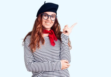 Fransız şapkası takan genç ve güzel bir kadın gülümseyen bir bereyle mutlu bir şekilde elini ve parmağını yana doğru uzat. 