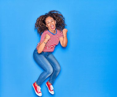 Orta yaşlı, güzel, İspanyol bir kadın. Günlük kıyafetler giyip mutlu gülümsüyor. İzole edilmiş mavi arka planda yüzünde gülümsemeyle zıplıyor