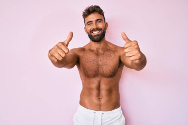 İspanyol asıllı genç adam elinde olumlu bir jest yaparak üstsüz duruyor. Gülümsüyor ve başarı için seviniyor. kazanan jest. 