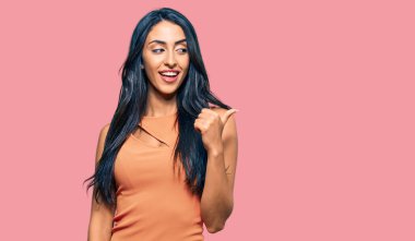 Yazlık elbise giyen, gülümseyen, gülümseyen güzel İspanyol kadın başparmağıyla yan tarafa bakıyor.. 