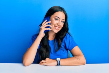 Güzel esmer bir kadın akıllı telefondan konuşuyor. Olumlu ve mutlu görünüyor. Kendine güvenen bir gülümsemeyle dişlerini gösteriyor. 