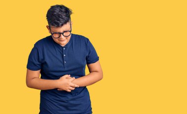 Küçük çocuk günlük kıyafetler giyiyor ve elleri karnında gözlük takıyor çünkü hazımsızlık, acı verici bir hastalık kendini iyi hissetmiyor. Ağrı kavramı. 