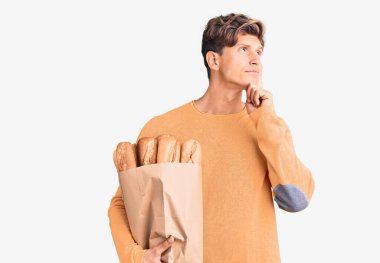 Elinde ekmek torbası olan yakışıklı bir genç adam ciddi bir yüz ifadesiyle eli çenesinde soru sormayı düşünüyor, kafa karıştırıcı bir fikir hakkında düşünceli. 