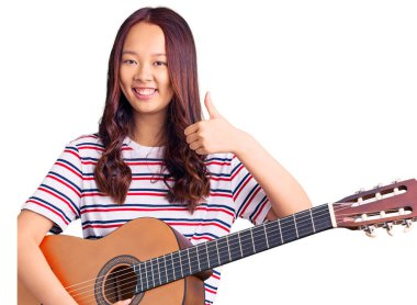 Genç güzel Çinli kız klasik gitar çalıyor mutlu ve pozitif gülümsüyor, başparmağıyla mükemmel ve onay işareti yapıyor. 