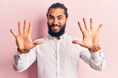 Genç Arap adam gündelik giysiler giyer ve parmaklarını on numarayla gösterir ve gösterirken kendinden emin ve mutlu gülümserdi.. 