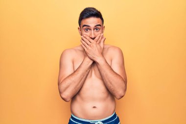 Sarı arka planda duran kolsuz tişört giyen sakallı yakışıklı genç adam ağzını yanlışlıkla ellerle kapatarak şok etti. Gizli konsept.