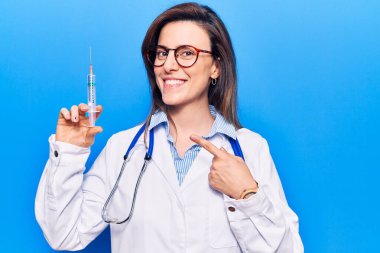 Doktor steteskopu olan genç ve güzel bir kadın elinde şırıngayla gülümsüyor. 