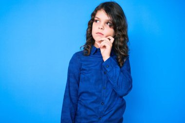 Uzun saçlı, hoş İspanyol çocuk. Günlük kıyafetler giyiyor. Ciddi bir yüz ifadesi var. Elleri çenesinde soru sormayı düşünüyor. 