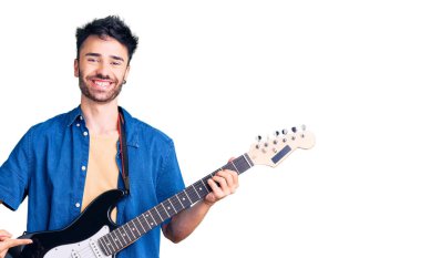 Elektro gitar çalan genç İspanyol adam mutlu bir şekilde elini ve parmağını işaret ediyor. 