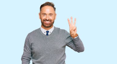 İş kıyafetleri giymiş yakışıklı orta yaşlı bir adam üç numarayı gösterip işaret ederken kendinden emin ve mutlu bir şekilde gülümsüyor.. 
