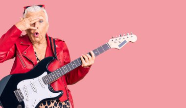 Son sınıf güzeli, mavi gözlü, gri saçlı, modern görünümlü, elektro gitar çalan, yüzünü ve gözlerini kapayan, utangaç bir ifadeyle parmaklarından bakan bir kadın.. 