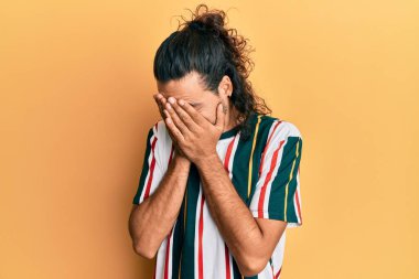 Uzun saçlı, sıradan kıyafetler giyen, suratını ellerle örten ve ağlayan yakışıklı bir genç. depresyon kavramı. 