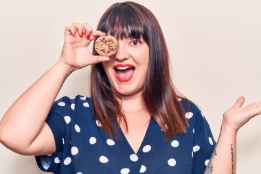 Elinde çikolatalı kurabiye tutan genç bir kadın mutlu bir gülümsemeyle başarıyı kutluyor ve kazanan el kaldırarak ifade ediyor. 