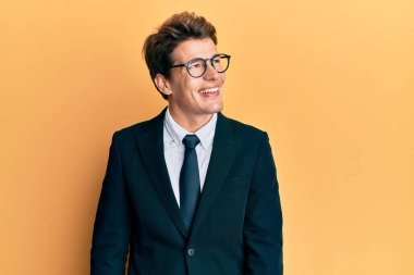 İş elbisesi ve kravat takan yakışıklı beyaz bir adam yüzünde gülümsemeyle yan yana bakıyor, doğal bir ifade. Kendinden emin gülen. 