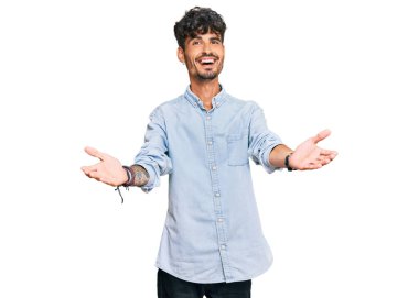 Gündelik giysiler giymiş genç İspanyol adam kameraya bakıp sarılmak için kollarını açmış gülümsüyor. Mutluluğu kucaklayan neşeli bir ifade.. 