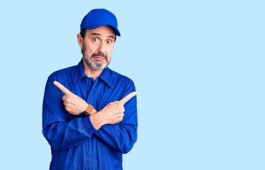 Orta yaşlı, tamirci üniforması giyen yakışıklı adam her iki tarafı da parmaklarıyla işaret ediyor. Farklı yönlere bakıyor. 