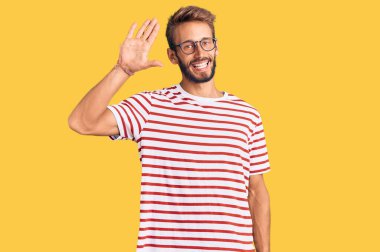 Sakallı, sıradan kıyafetler ve gözlüklü yakışıklı adam merhaba diyor mutlu ve güler yüzlü, dostça bir jest. 