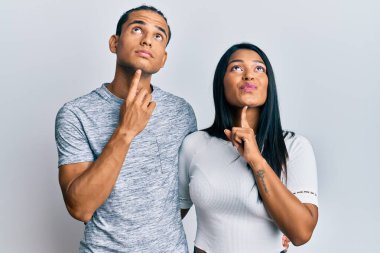 Gündelik giysiler giyen genç latin çift şüpheye yoğunlaşmışlar, parmakları çenelerinde ve yukarı bakıp merak ediyorlar. 