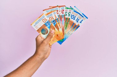 İspanyol eli İsviçre frangı banknotlarını soyutlanmış pembe arka planda tutuyor.