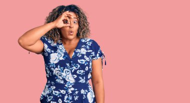 Genç Afro-Amerikan artı cüsseli kadın normal giyiniyor. Şaşırmış bir yüz ve parmaklarından bakan bir gözle şaşırmış bir hareket yapıyor. İnançsız ifade. 