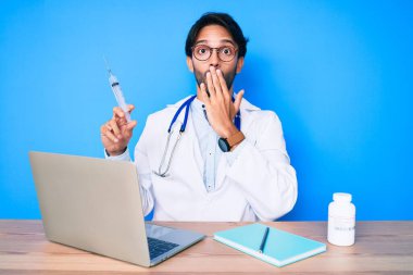 Klinikteki yakışıklı İspanyol doktor elinde şırıngayla ağzını kapatıyor, şok geçiriyor ve hata yapmaktan korkuyor. şaşırmış ifade 