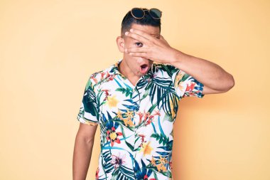 Yazlık giysiler giymiş genç, yakışıklı Latin bir adam. Şoka girmiş, yüzünü ve gözlerini kapamış, utanmış bir ifadeyle parmaklarından bakıyor.. 