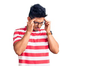 Yakışıklı Latin Amerikalı genç adam gündelik kıyafetler giyiyor ve elleri kafasında gözlük takıyor, stresten baş ağrısı çekiyor. migren ağrısı. 