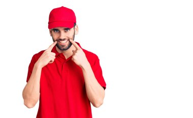 Sakallı, teslimat üniforması giyen, ağzı açık gülümseyen, parmakları işaret eden ve neşeli gülümsemeye zorlayan genç yakışıklı bir adam. 