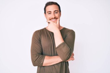 Sıradan kıyafetler giyen, kameraya kendinden emin, kolları çapraz ve çenesi havada gülümseyen genç yakışıklı bir adam. Olumlu düşünmek. 