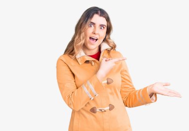 Gündelik giysiler giyen genç beyaz kadın kameraya hayret ediyor ve gülümsüyor.. 