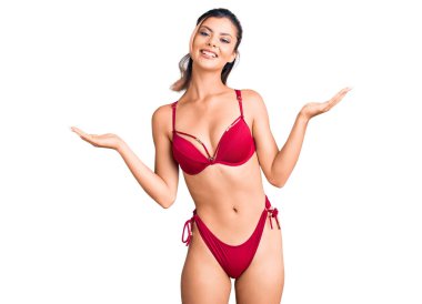 Bikini giyen genç ve güzel bir kadın gülümsüyor. İki elini de açık tutuyor. Karşılaştırma ve reklam karşılaştırması yapıyor. 