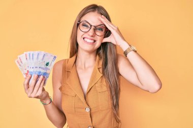 Elinde Kolombiya pezosu tutan genç sarışın kız. Kafası karışık, şaşırmış ve sinirli bir yüzü var. 