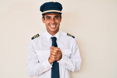 Ellerini kavuşturup gülümseyen ve rahat gülümseyen İspanyol pilot üniforması giyen genç bir adam. Başarı ve iyimserlik 