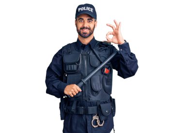 Polis üniforması giyen genç İspanyol adam copunu tutuyor. Parmaklarıyla imza atıyor, gülümseyerek mükemmel bir sembol oluşturuyor. 