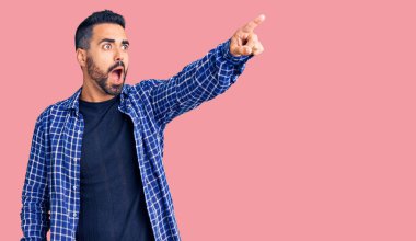 Gündelik giysiler giymiş genç İspanyol bir adam parmağıyla işaret ederek şaşırmış, ağzı açık, şaşırmış, ön tarafta bir şey var. 