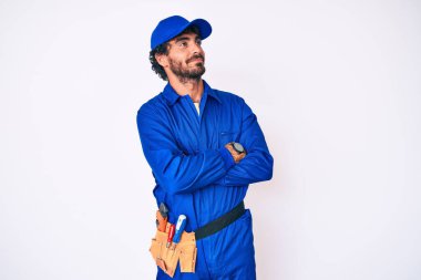 Kıvırcık saçlı ve ayı gibi giyinen yakışıklı genç adam kollarını kavuşturmuş ve kendinden emin bir şekilde yan tarafa bakıyor. 