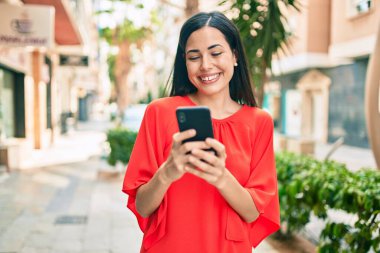 Genç Latin kız şehirde akıllı telefon kullanarak mutlu bir şekilde gülümsüyor..