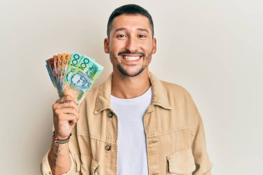 Dövmeleri olan yakışıklı bir adam. Elinde Avustralya doları var. Olumlu ve mutlu görünüyor. 