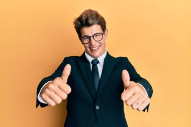 İş elbisesi giyen ve kravat takan yakışıklı beyaz adam. Elle olumlu jest yapmayı onaylıyor. Gülümsüyor ve başarı için seviniyor. kazanan jest. 