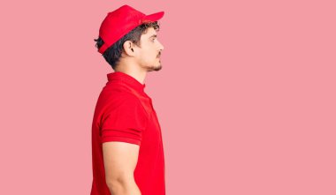 Kıvırcık saçlı, teslimat üniforması giyen rahat bir görünüm takınan, kendine güveni tam, doğal bir yüzle poz veren genç yakışıklı bir adam.. 