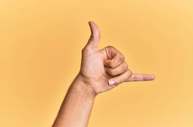 Beyaz adamın eli ve kolu sarı izole arka planda. Hawai Shaka selamlama hareketi, telefon ve iletişim sembolü. 