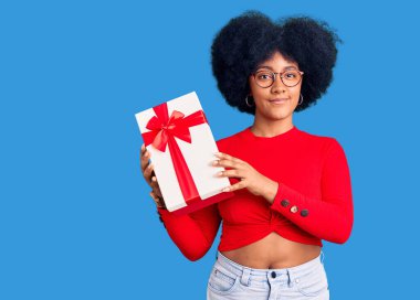 Elinde hediye tutan Afro-Amerikan genç kız yüzünde ciddi bir ifadeyle rahatlamış. Basit ve doğal bir şekilde kameraya bakıyorsun.. 