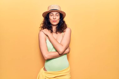 Mayo ve yaz şapkası takan genç ve güzel İspanyol bir kadın mutlu ve olumlu bir şekilde kendine sarılıyor, kendinden emin gülümsüyor. Sevgi ve özgüven. 