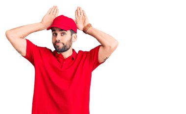 Sakallı, teslimat üniforması giyen, tavşan kulağı takan, avuçlarıyla alaycı ve şüpheci görünen genç yakışıklı bir adam. Paskalya tavşanı konsepti. 