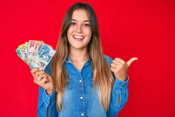 Piękna Biała Kobieta Trzyma Australijskie Dolary Wskazując Kciuk Góry Bok — Zdjęcie stockowe