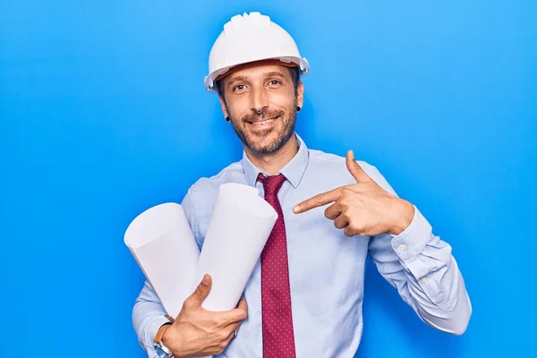 Jovem Homem Bonito Vestindo Arquiteto Hardhat Segurando Plantas Sorrindo Feliz — Fotografia de Stock