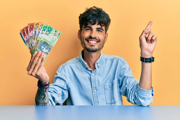 Joven Hispano Sosteniendo Dólares Australianos Sentado Mesa Sonriendo Feliz Señalando — Foto de Stock