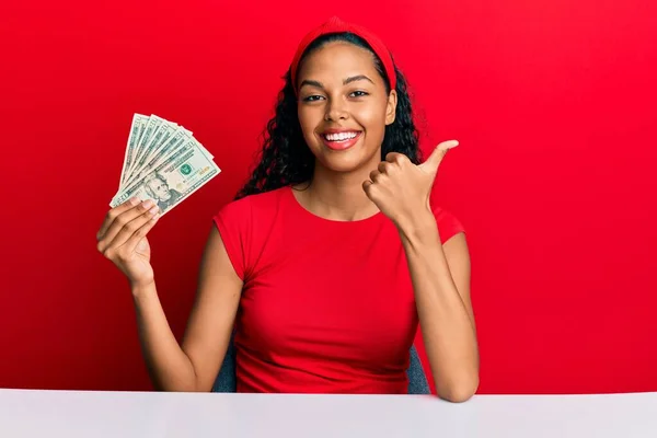 Jovem Afro Americana Segurando Dólares Sentados Mesa Apontando Polegar Para — Fotografia de Stock